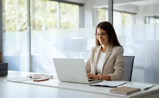 Businesswoman working on a laptop in a bright, modern office environment while reviewing B2B targeting or customer insights.