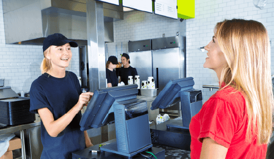 Franchise employee at a quick-service counter greeting a customer, illustrating localized, store-level engagement within multi-location marketing programs.