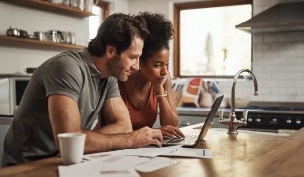 Couple reviewing home service paperwork together at a kitchen counter while using a laptop, representing the decision-making moments digital campaigns aim to influence.