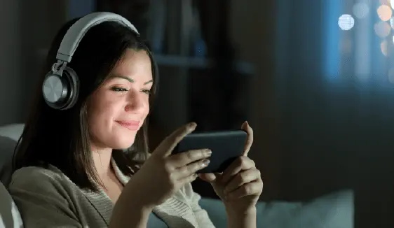 Woman listening with over-ear headphones while using her mobile phone at home, demonstrating how programmatic audio campaigns reach listeners across streaming music, podcasts, and digital radio.